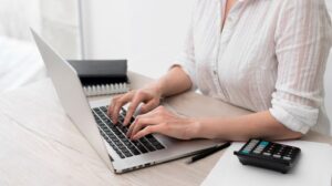 a woman using a laptop, with a calculator and a pen nearby